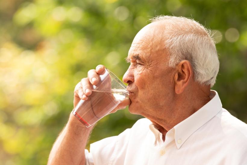 Oudere man drinkt glas water tegen uitdroging