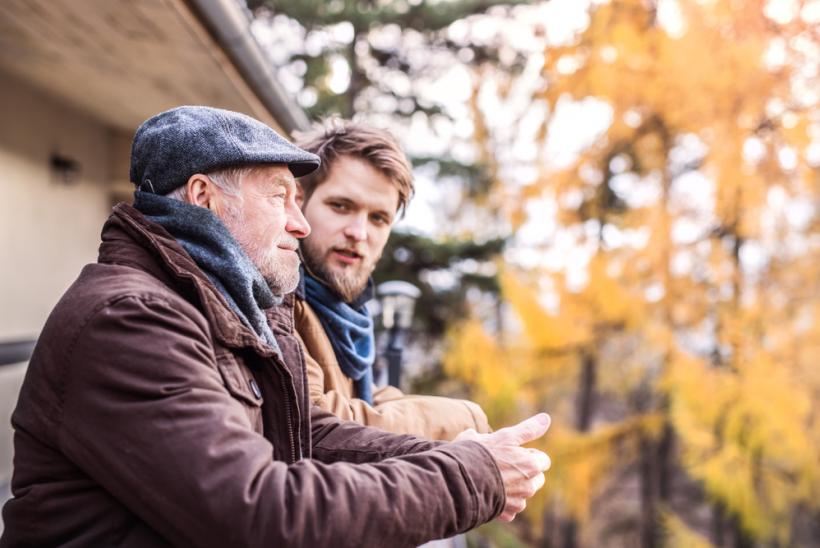 Een oudere en een jongere man zitten buiten bij een huis in de herfst